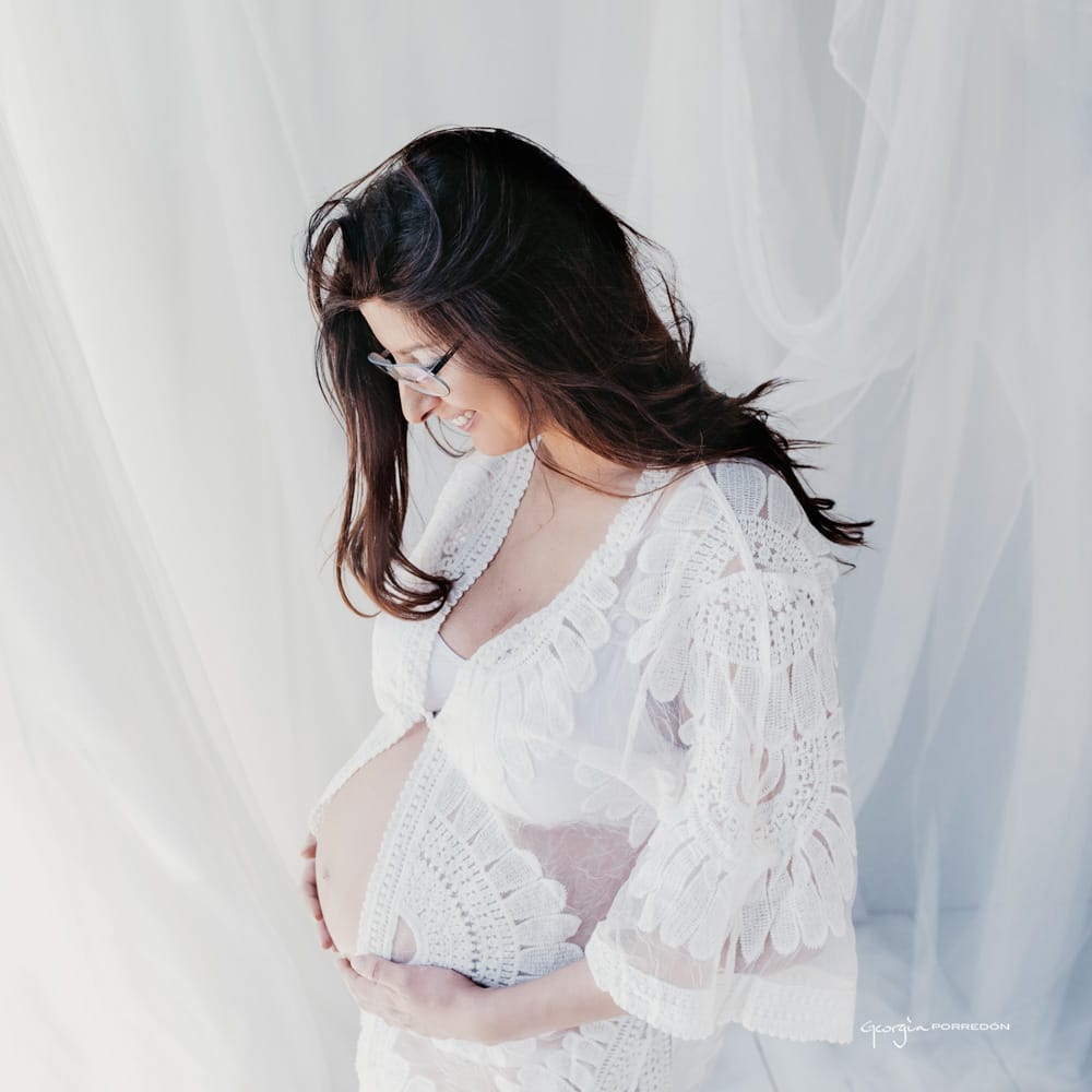 futura mare embarassada mirant cap avall amb un vestit blanc transparent