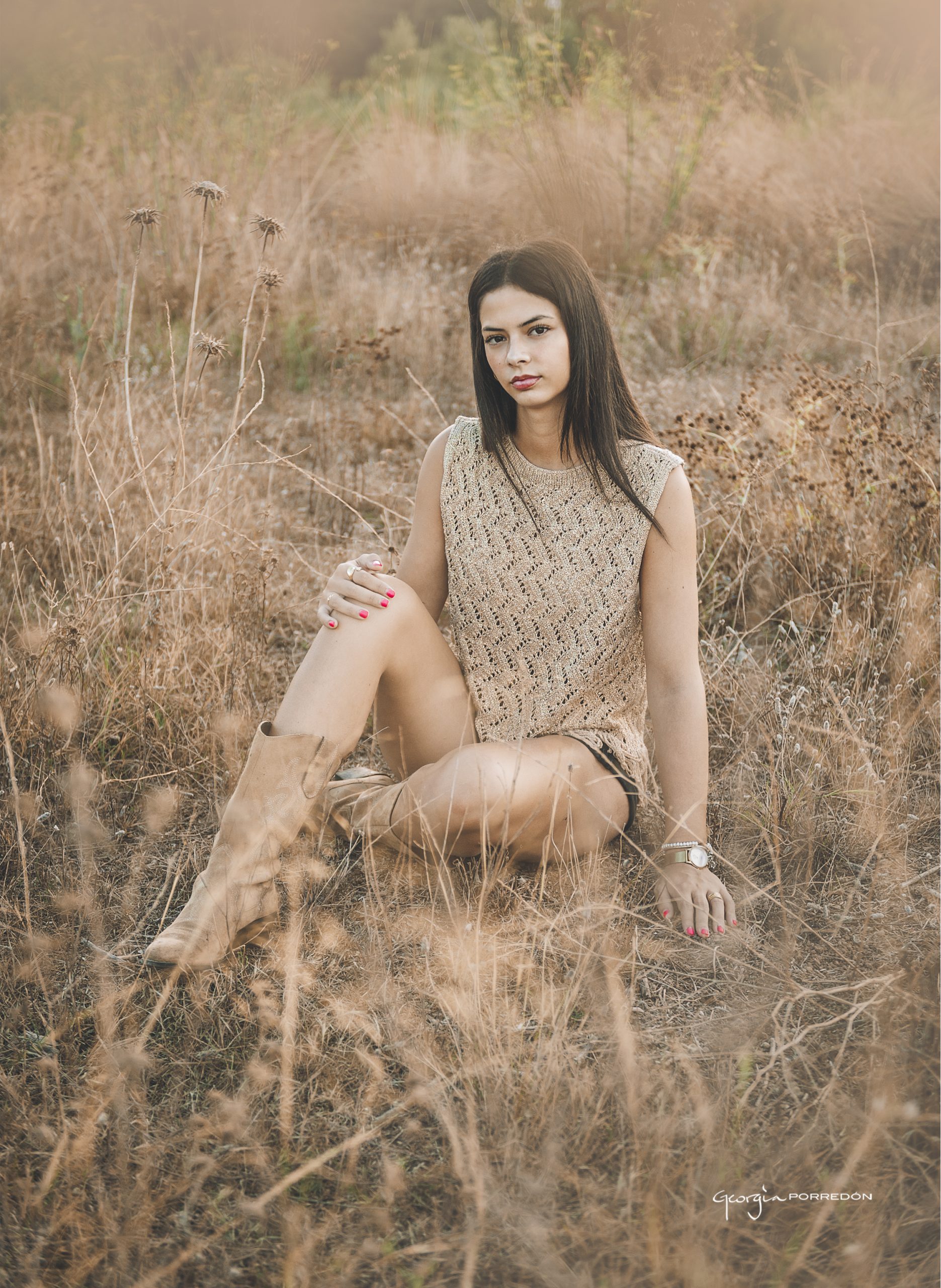 retrato tipo editorial de adolescente para su sesión de reportaje exterior realizado por Georgia Porredon. Está sentada en el suelo con shorts y botas camperas con un jersey de crochet dorado y es una fotografia que te lleva a un paisaje árido. Sessió de fotografia per a adolescents a Granollers amb estil editorial